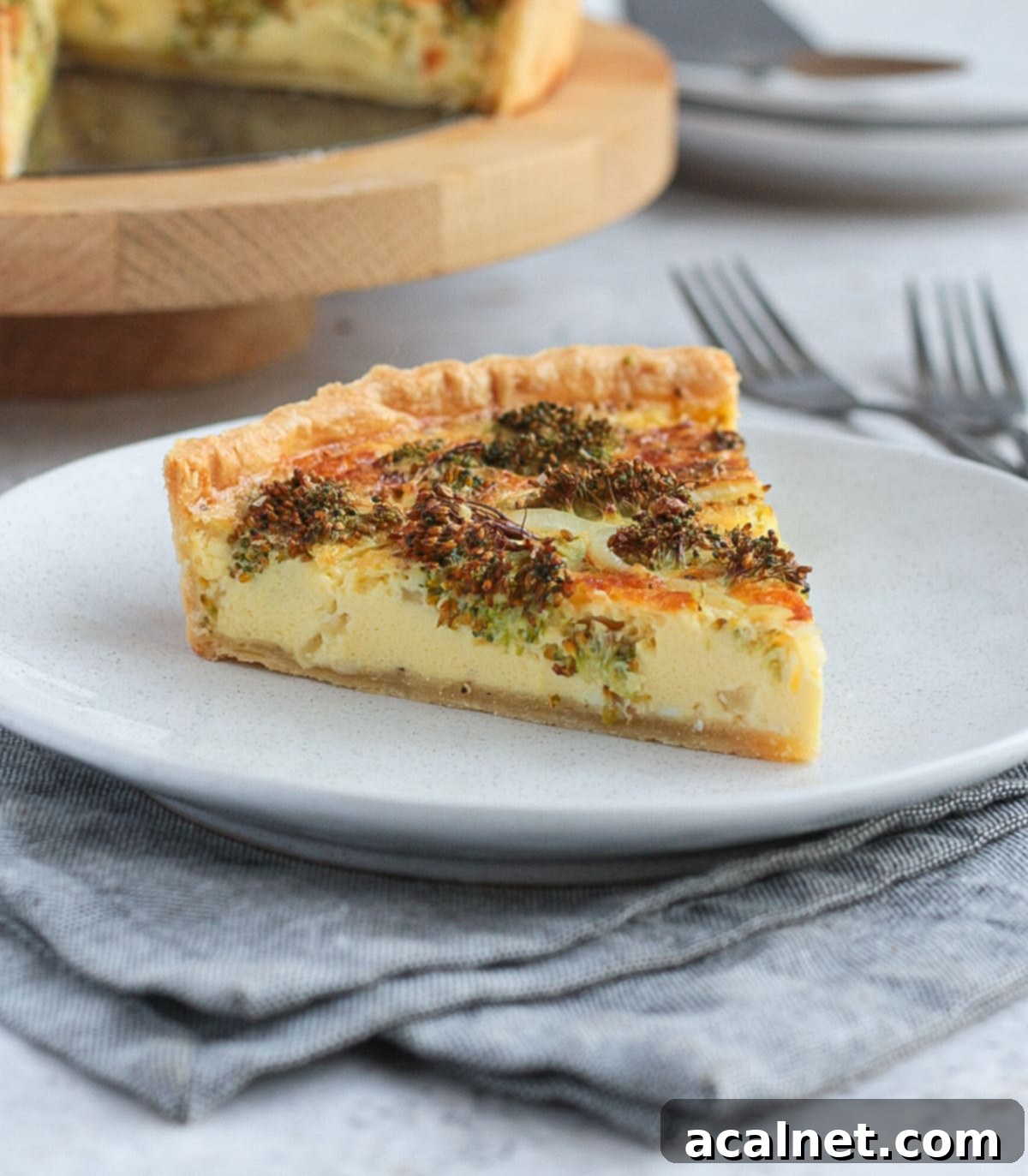 One slice of Broccoli Cheddar Quiche on a white plate, showcasing the flaky crust and rich filling.