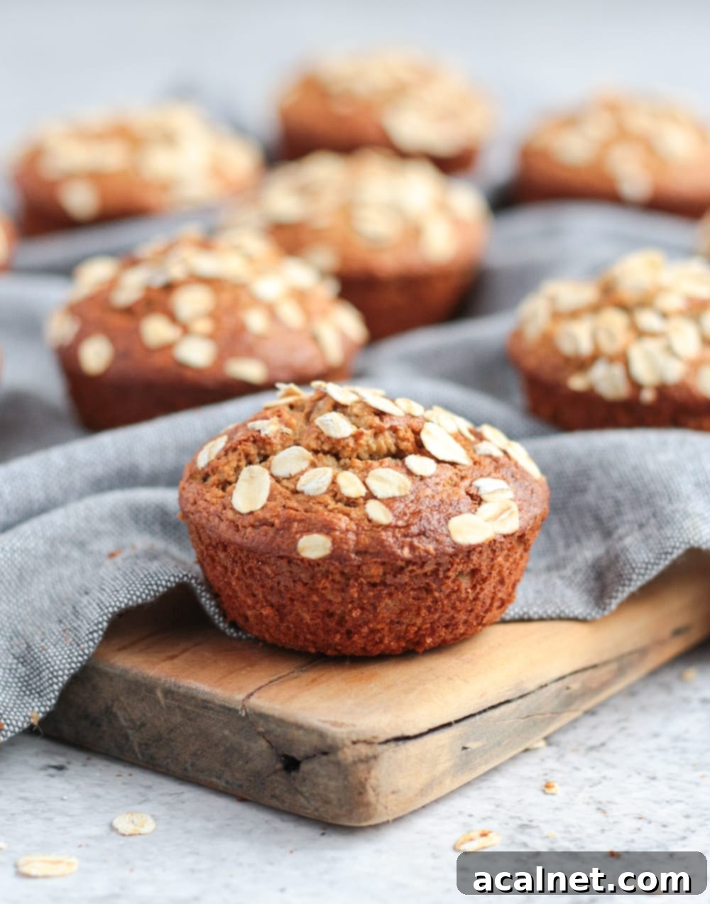 A close-up of a single oatmeal banana muffin on a wooden cutting board, showcasing its fluffy texture and golden crust.