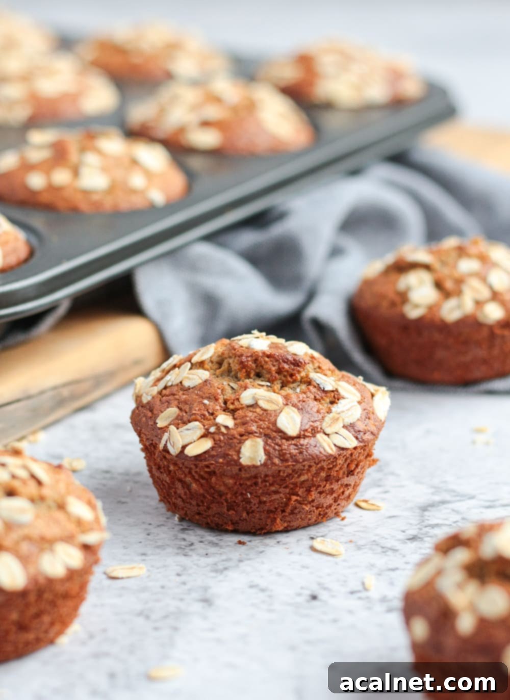 A close-up of a single oatmeal banana muffin, perfectly risen and golden, sitting next to a muffin pan.