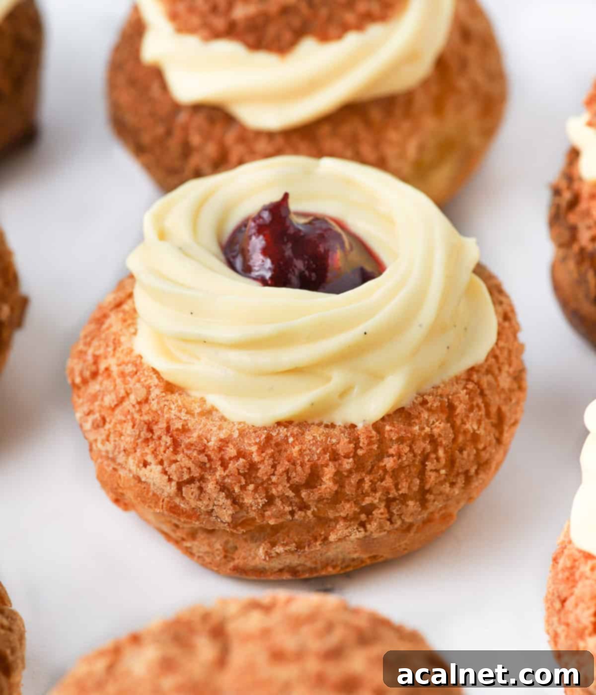 Vanilla custard piped over a choux sliced in half and filled with jam.