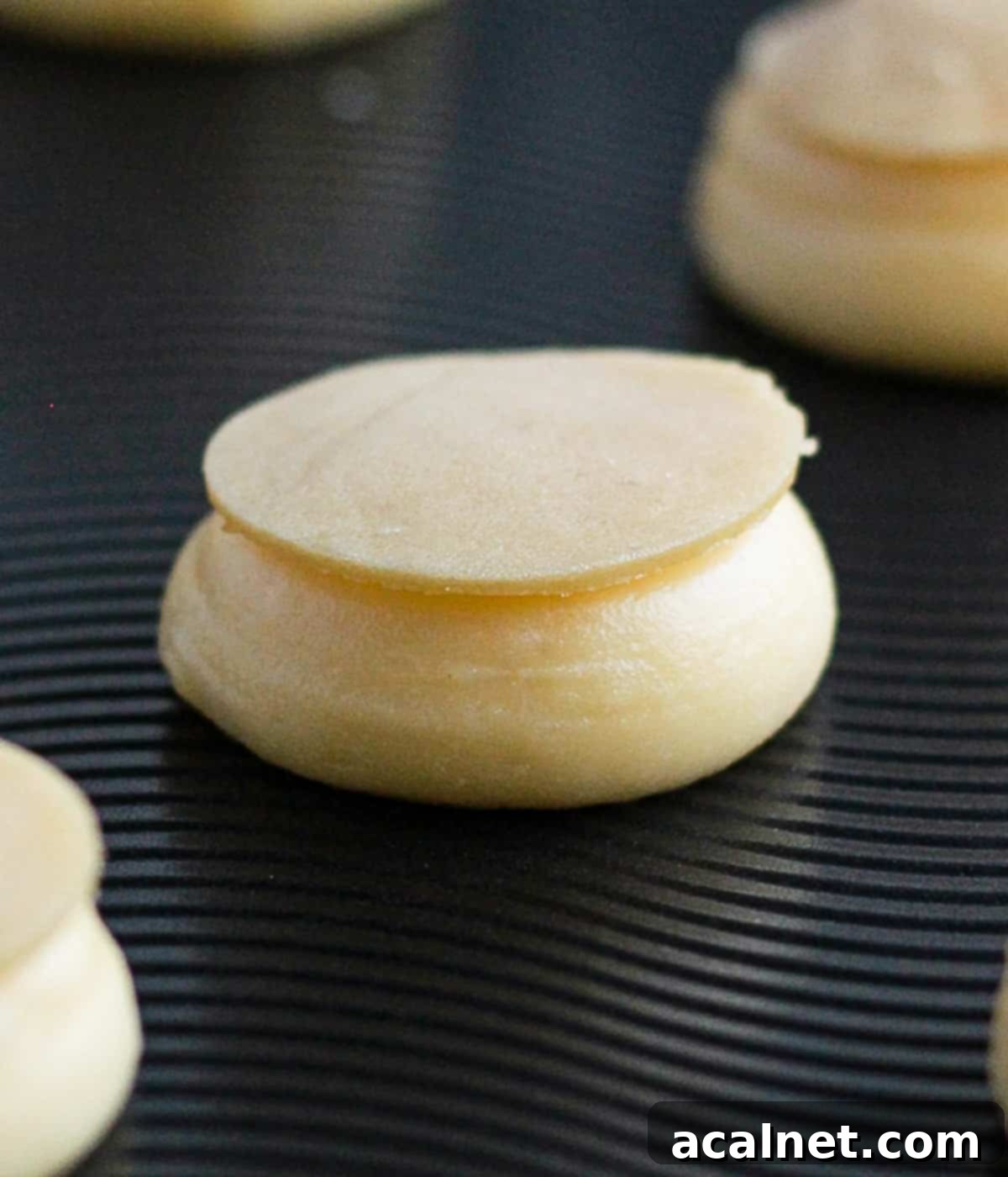 Disk of craquelin placed over a piped dollop of choux pastry on a baking tray.