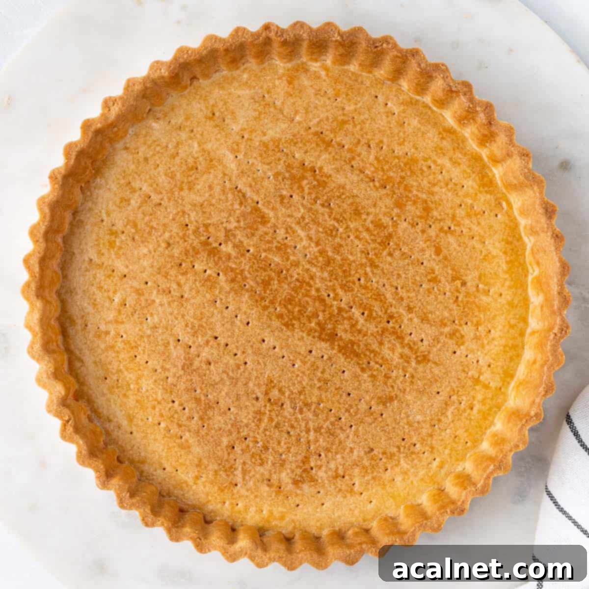 Fully blind baked tart crust seen from above. A golden-brown Pâte Sucrée shell, perfectly shaped within a fluted tart pan.