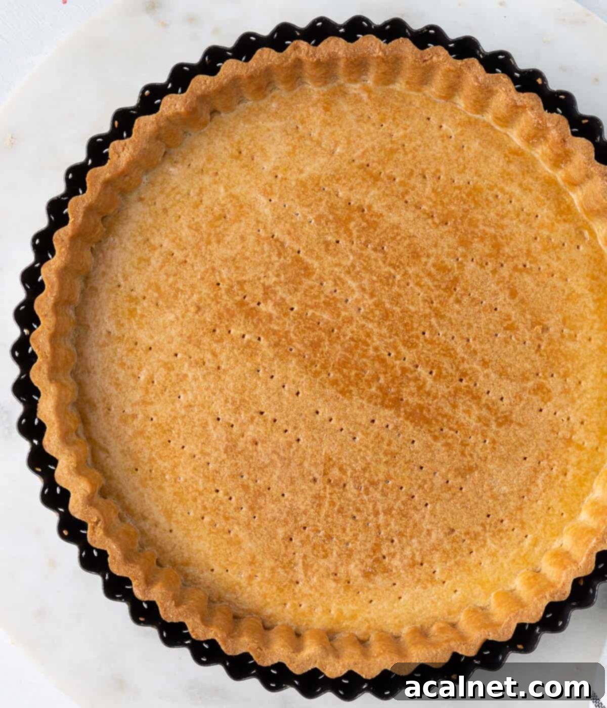 Baked tart shell in the tart pan seen from above, golden and ready for filling.