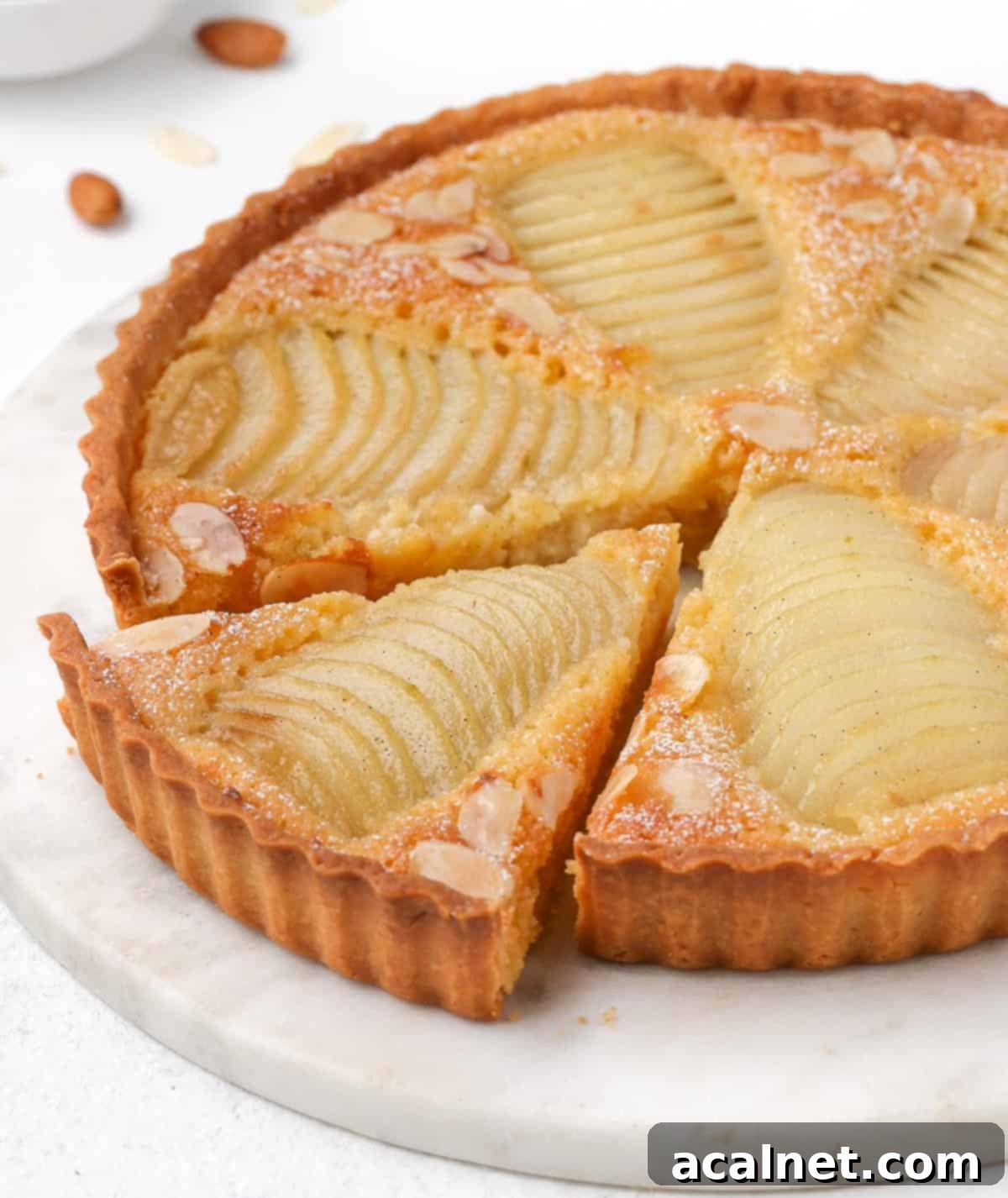 Side view of a pear frangipane tart with a slice cut out, showcasing the perfect Pâte Sucrée crust.