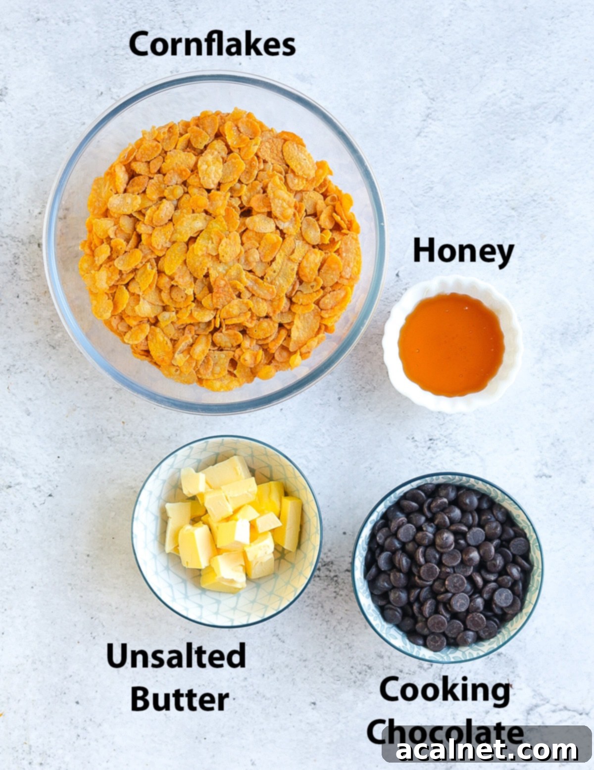 A flat lay image displaying the four simple ingredients for chocolate cornflake cakes: cornflakes, honey, butter, and dark chocolate.