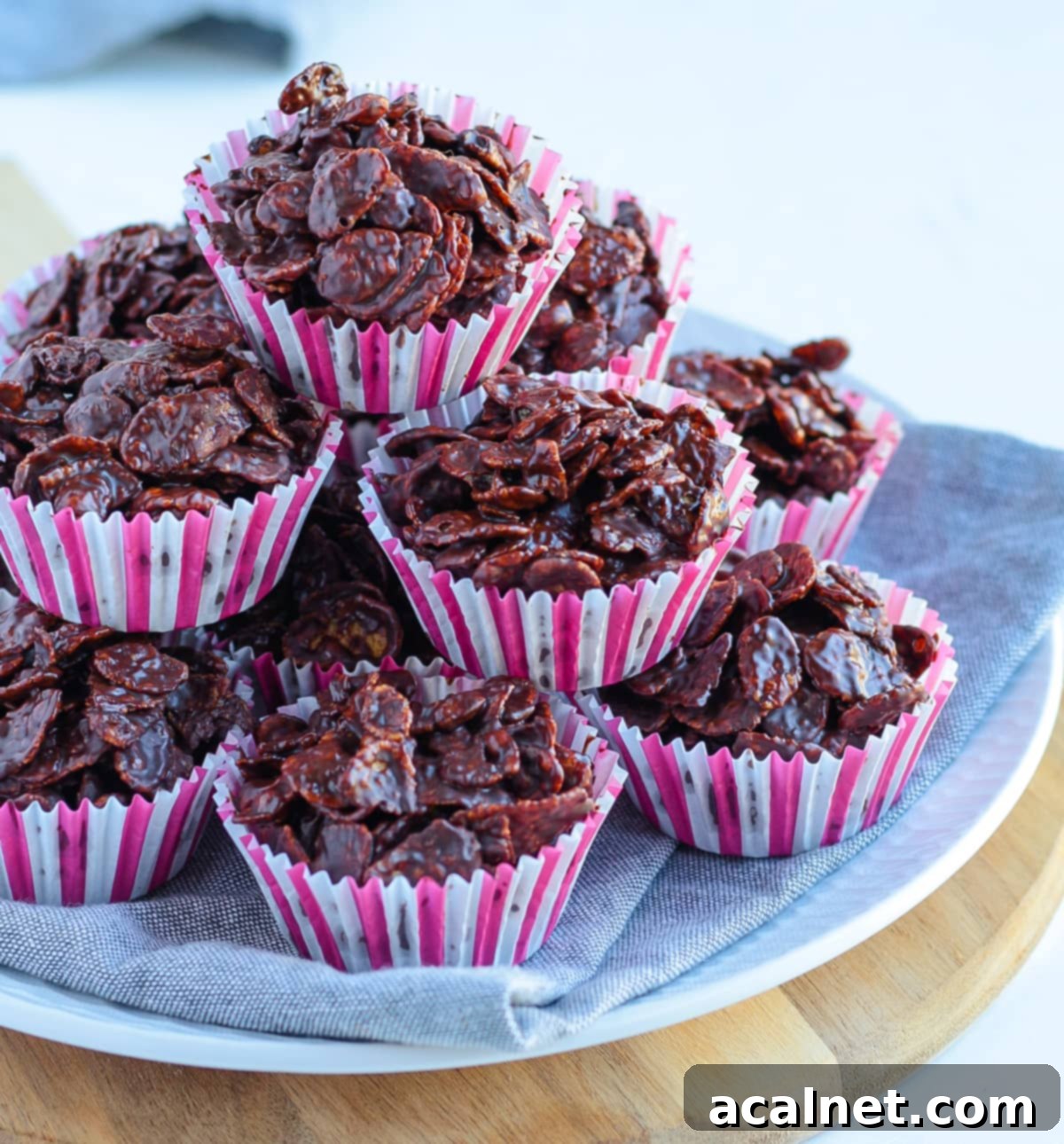 A stack of golden chocolate cornflake cakes arranged on a grey napkin and small wooden board, highlighting their inviting texture.