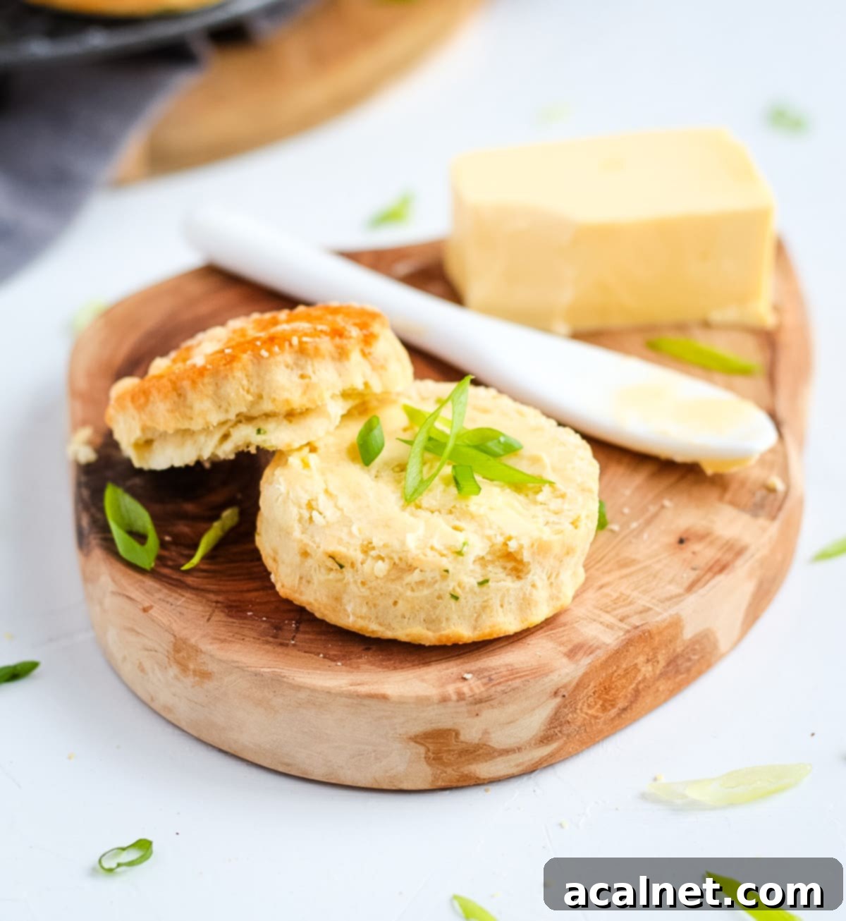 Scone sliced in half with butter and fresh sliced spring onion, over a wooden tray
