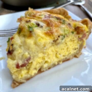 A wedge of quiche on a plate with the quiche dish in the background.