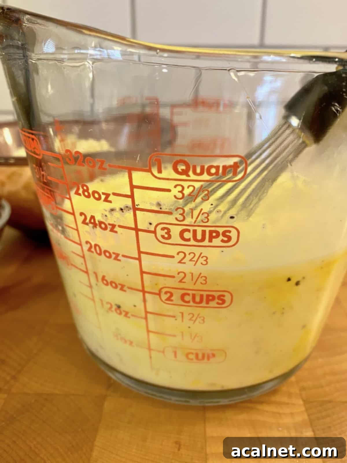 Eggs and milk whisked together in a glass measuring cup, ready for the quiche filling.