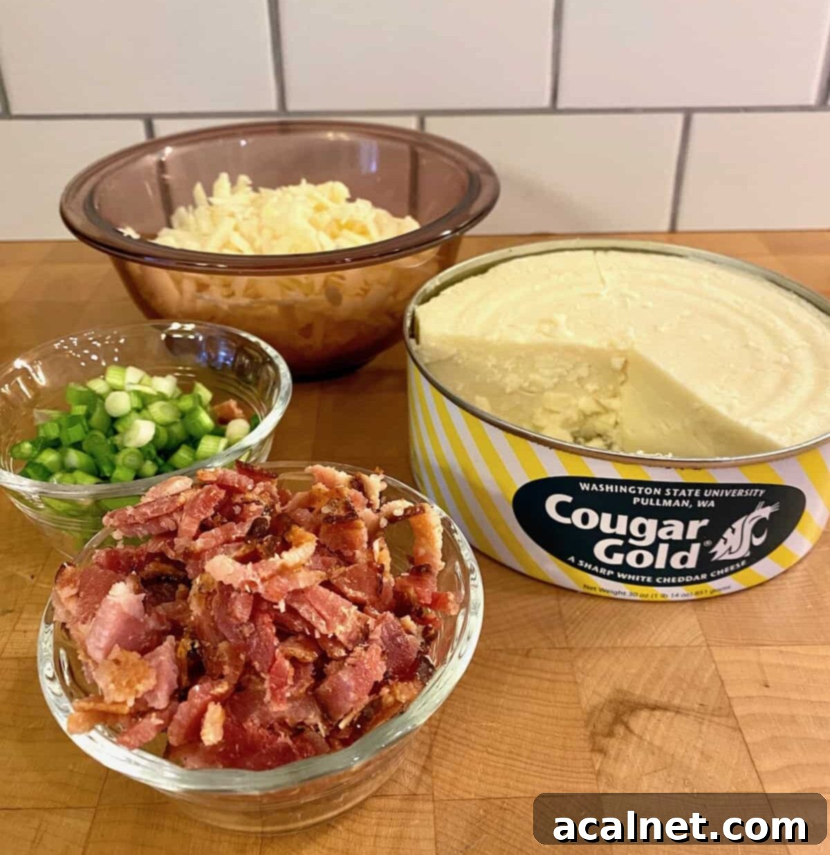 Small bowls of cooked, diced bacon, sliced green onions, and shredded cheese, with an opened can of Cougar Gold on the side, showing prepared ingredients.