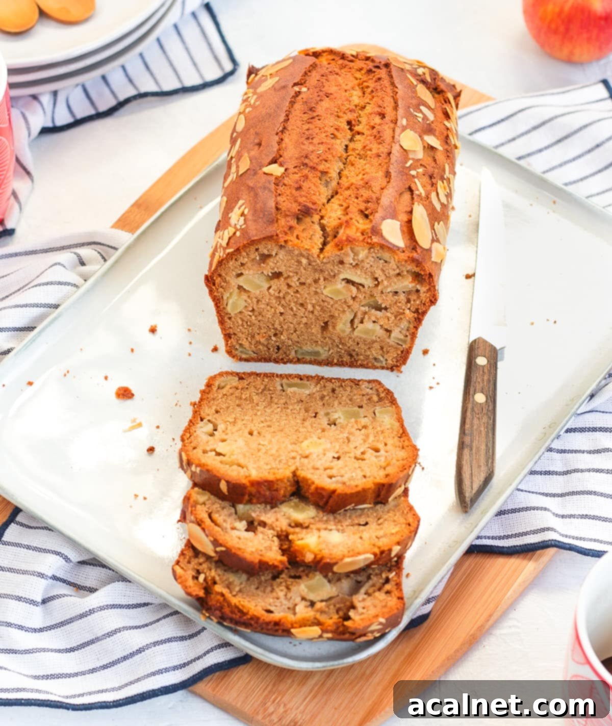 Baked apple loaf cake on a white rectangular plate with a few slices cut off.