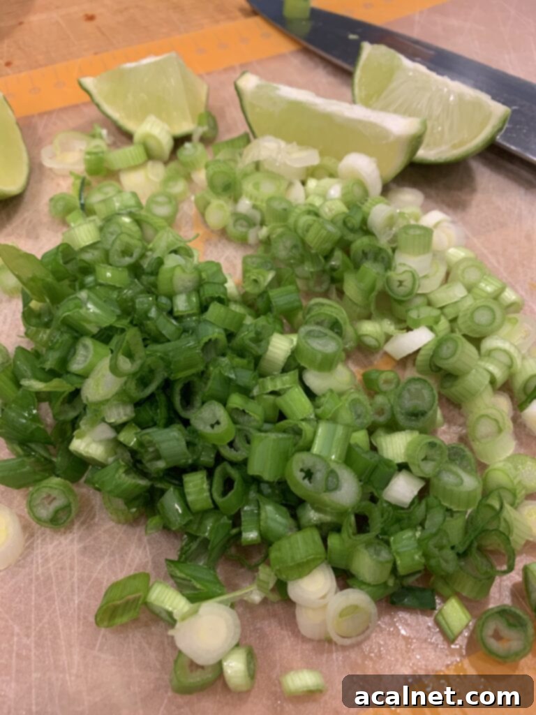 Chopped green onions and lime wedges on a cutting mat. 