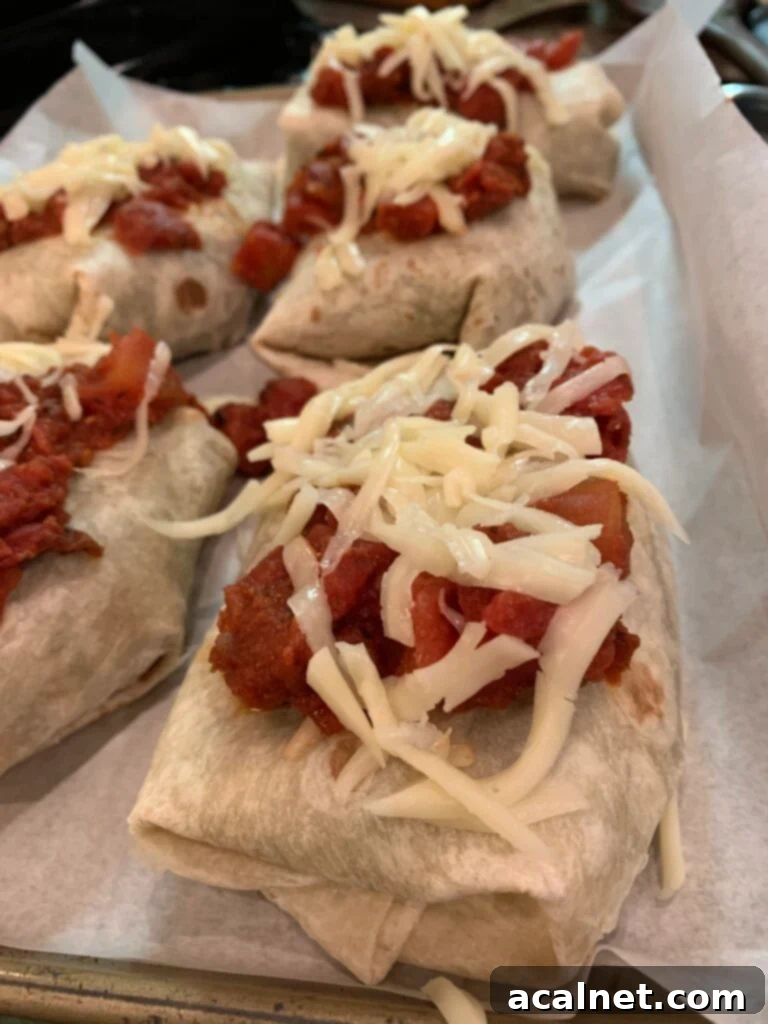 Burritos covered with tomato sauce and cheese on a baking dish. 