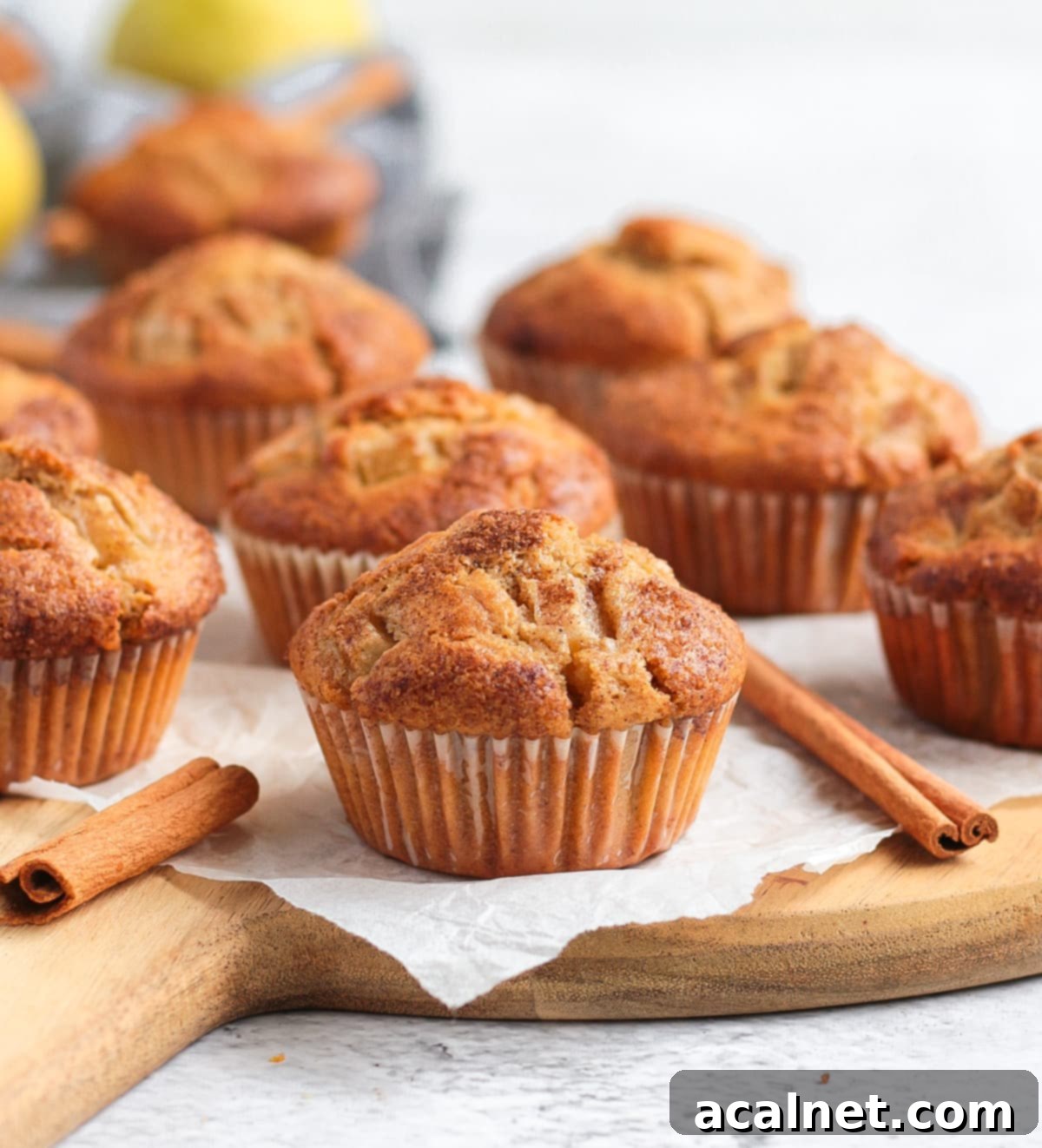 Warm Spiced Pear Muffins 7 A cluster of freshly baked spiced pear muffins arranged on a round wooden board with cinnamon sticks for garnish.