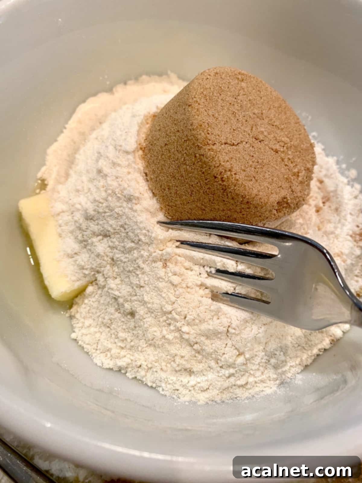 A fork blending together brown sugar, softened butter, and flour in a small bowl to create the initial stages of a streusel topping mixture.