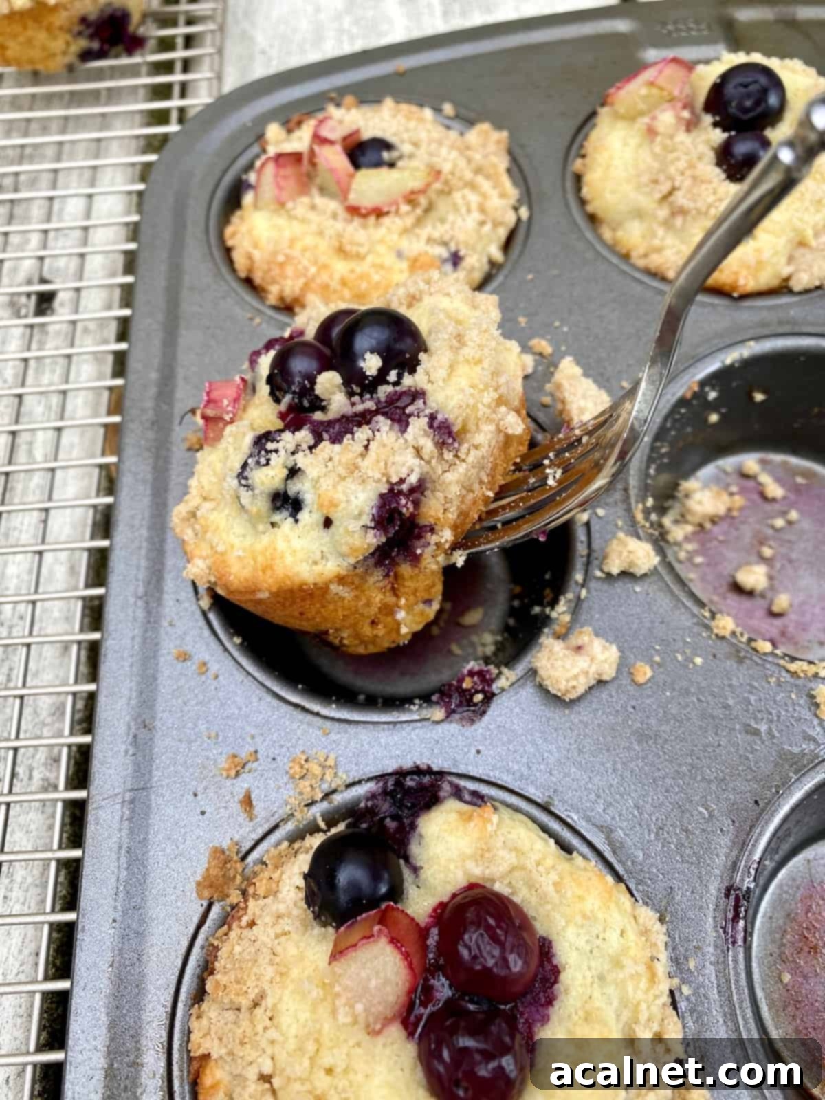 A fork carefully removing a freshly baked muffin from a muffin pan, showing the intact, crunchy streusel topping and tender muffin base.