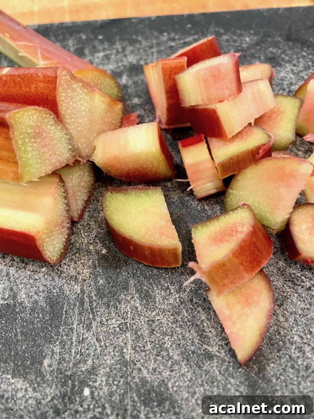 Freshly diced rhubarb pieces neatly arranged on a wooden cutting board, showcasing their vibrant pink and green colors, ready for baking.