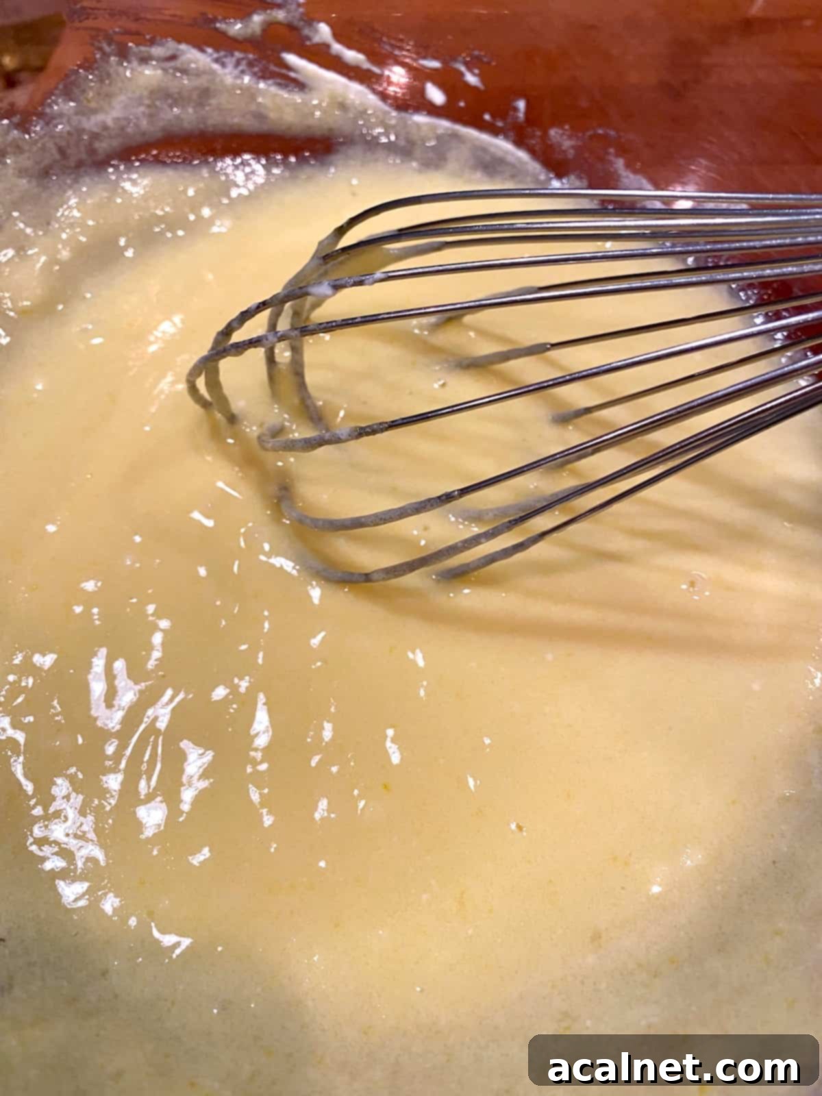 A whisk blending together eggs, granulated sugar, cooled melted butter, and plain Greek yogurt in a mixing bowl, creating a smooth and creamy wet ingredient mixture.