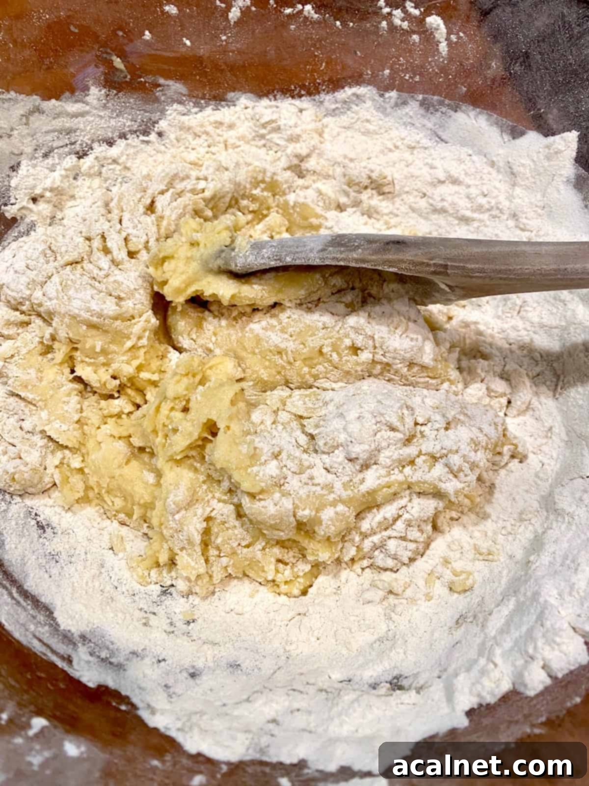 A wooden spoon carefully blending the dry flour mixture (flour, baking powder, baking soda, salt) into the wet ingredients in a large bowl, forming a cohesive muffin batter.