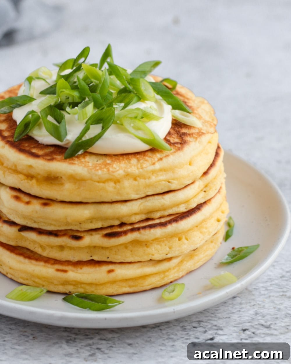 A stack of golden brown cheese pancakes topped with a dollop of sour cream and fresh spring onions