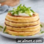 Close up on a stack of 4 fluffy savory cheese pancakes topped with sour cream and green onions on a white plate