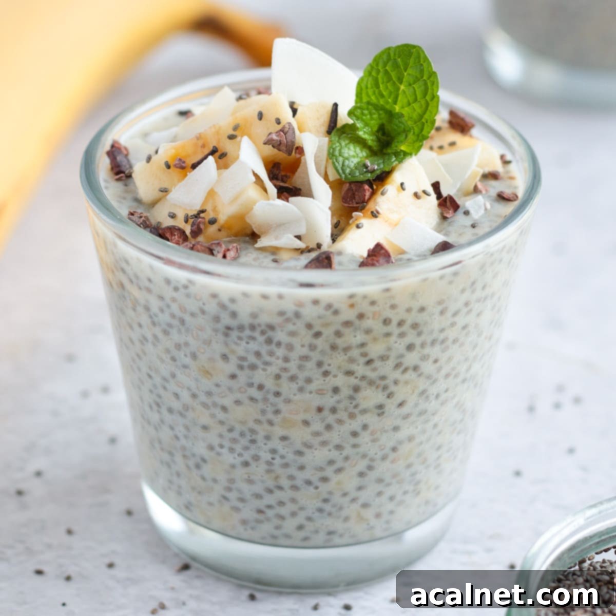 Banana Chia Seed Pudding in a small glass cup topped with coconut, bananas and mint