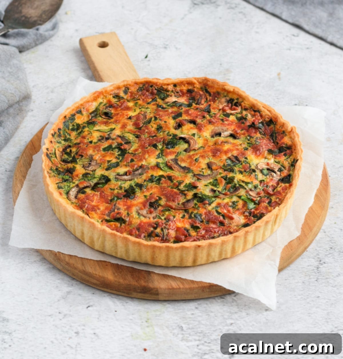 Quiche on a round wooden board over a grey surface