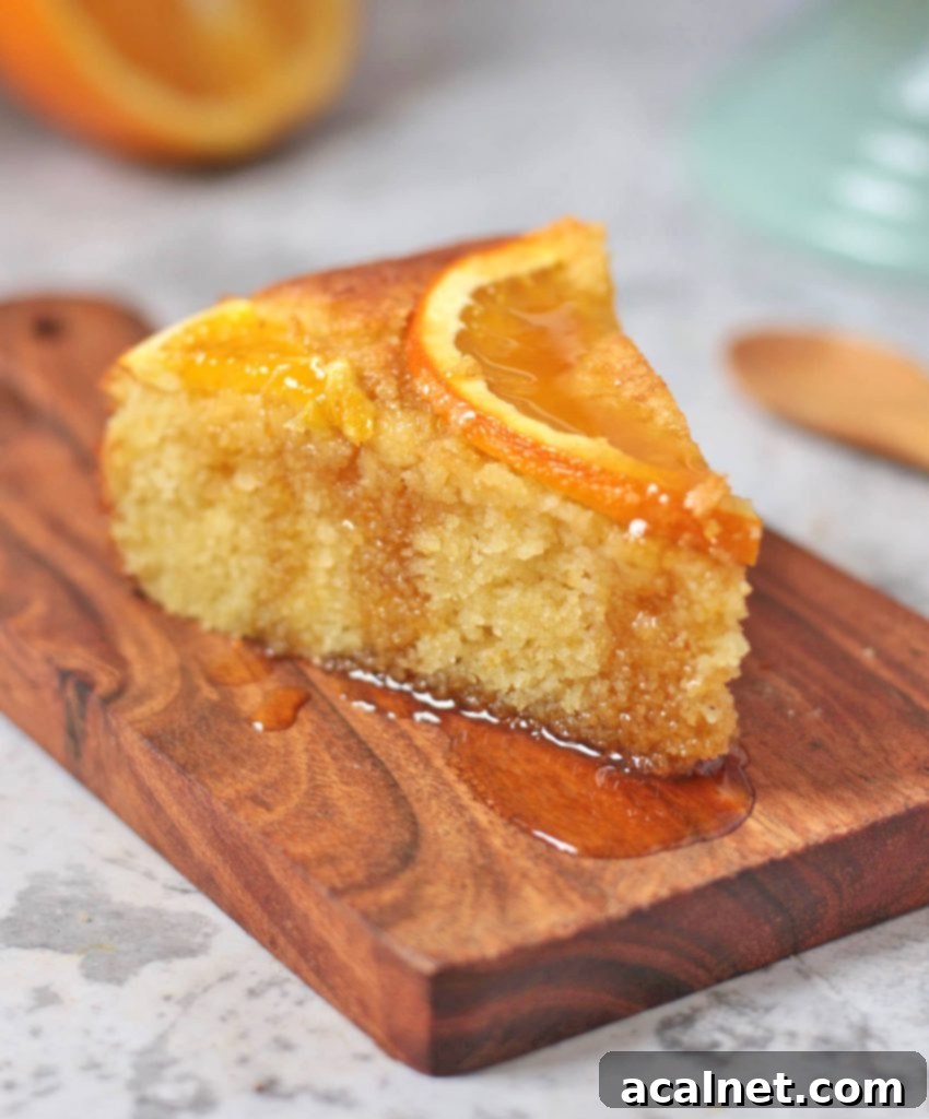 A single slice of Orange Semolina Cake artfully placed on a small wooden board, with syrup elegantly dripping down.