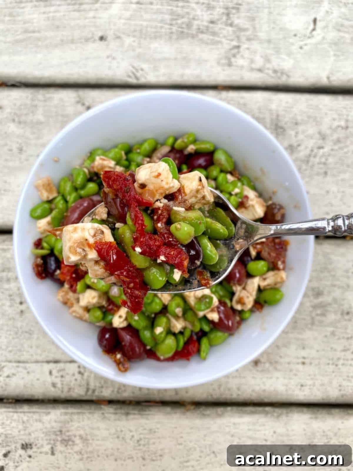 A small bowl brimming with edamame salad, with a serving spoon scooping out a portion, ready to be enjoyed or stored.