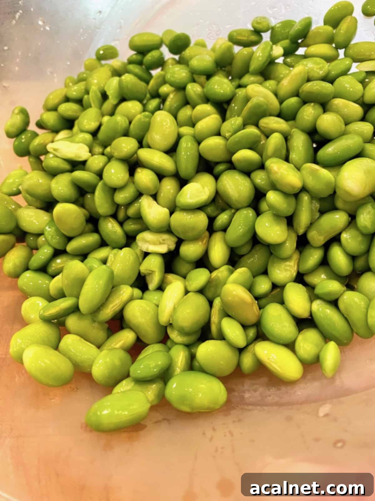 A mound of bright green, shelled edamame rests on a wooden cutting board, ready for use.