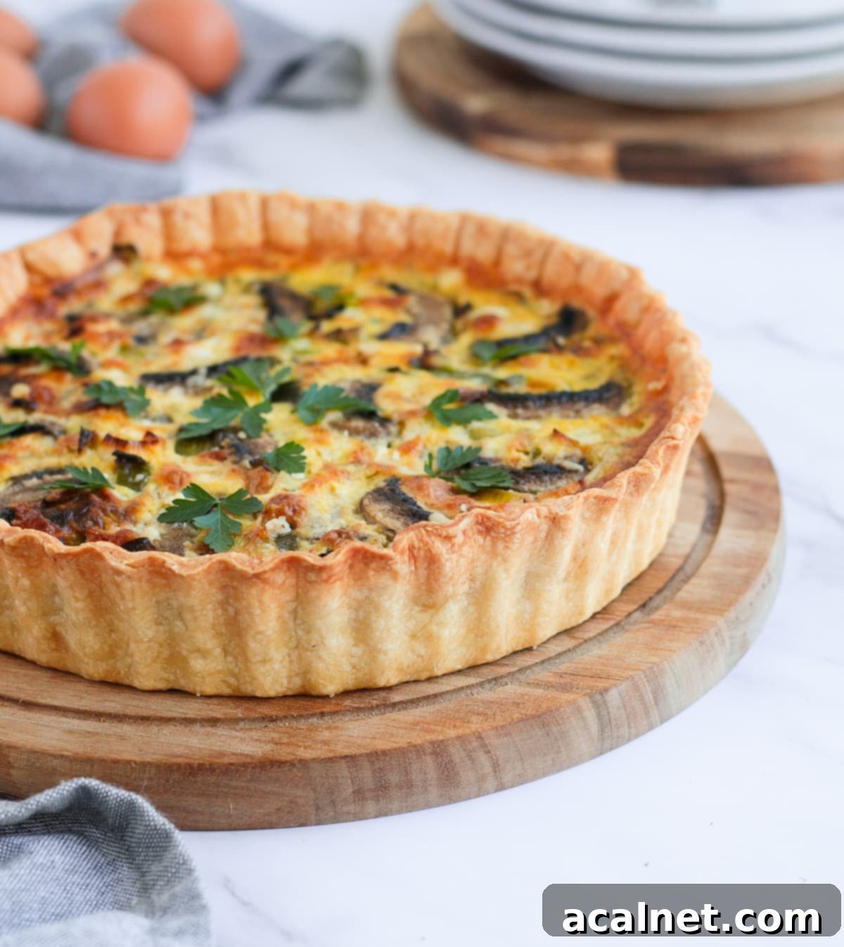Side view on the quiche over a wooden round board, showcasing the beautiful golden crust and creamy filling.