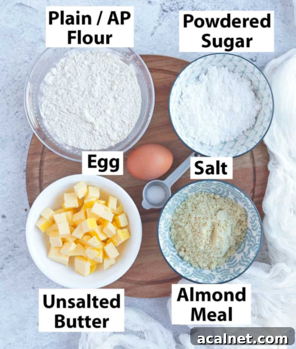 Pate Sucree Ingredients. A close-up shot of individual ingredients for Pâte Sucrée, including cubes of butter, powdered sugar, flour, almond meal, an egg, and a small pile of salt, arranged neatly on a surface.