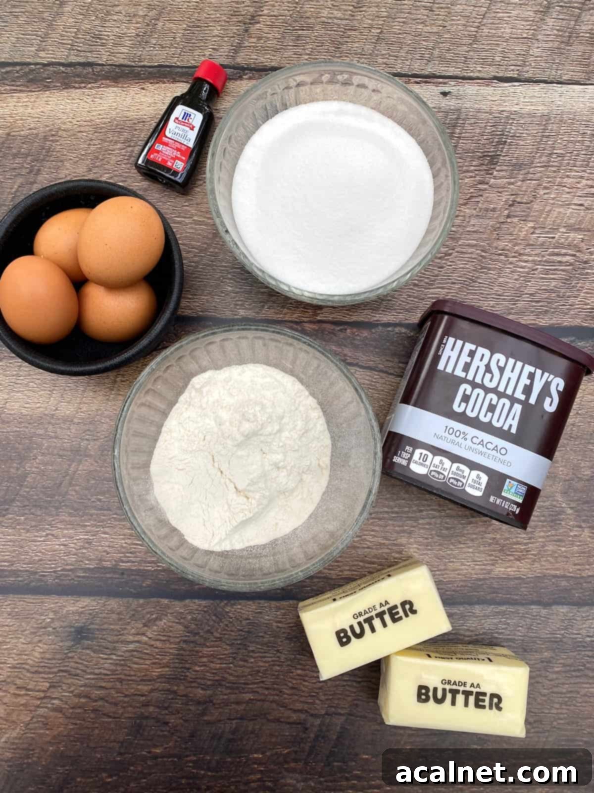 Eggs, vanilla extract, flour, sugar, cocoa powder and two sticks of butter displayed on a plank.