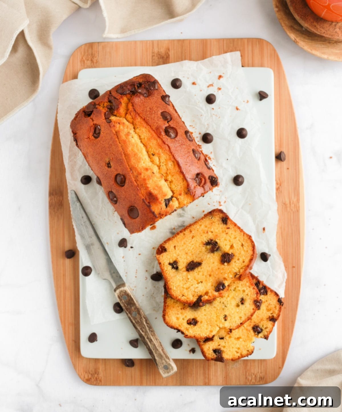 Close-up shot of a Chocolate Chip Loaf Cake on a white board over a wooden board from above, showing golden crust.