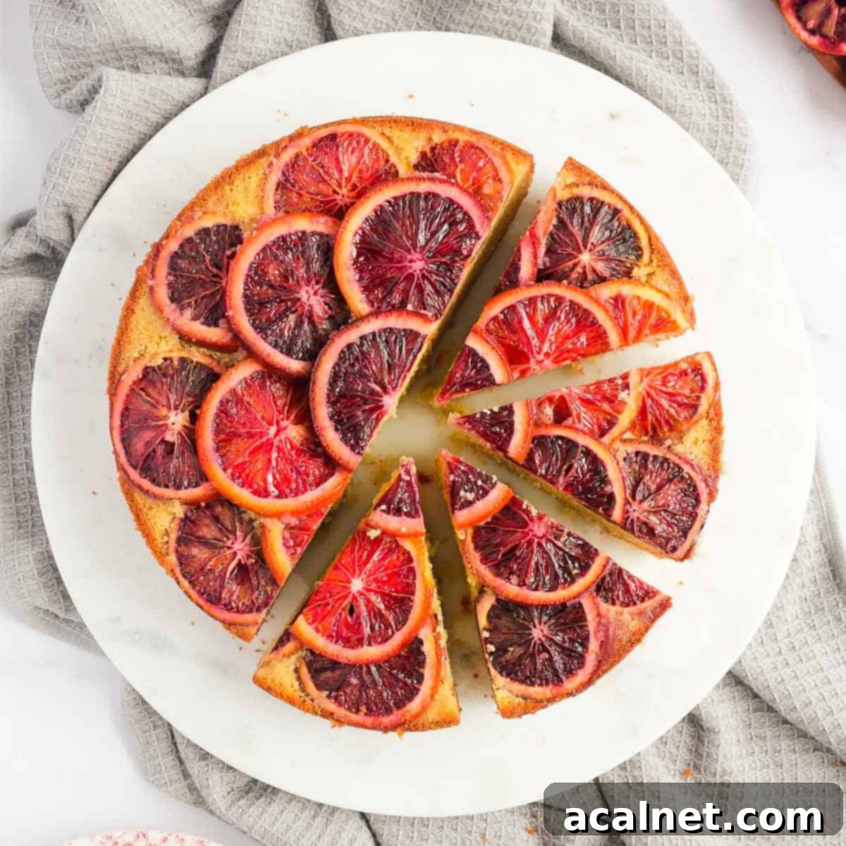 Flatlay photo of the cake on a round white board with 4 slices cut off, showcasing the beautiful caramelized blood orange topping.