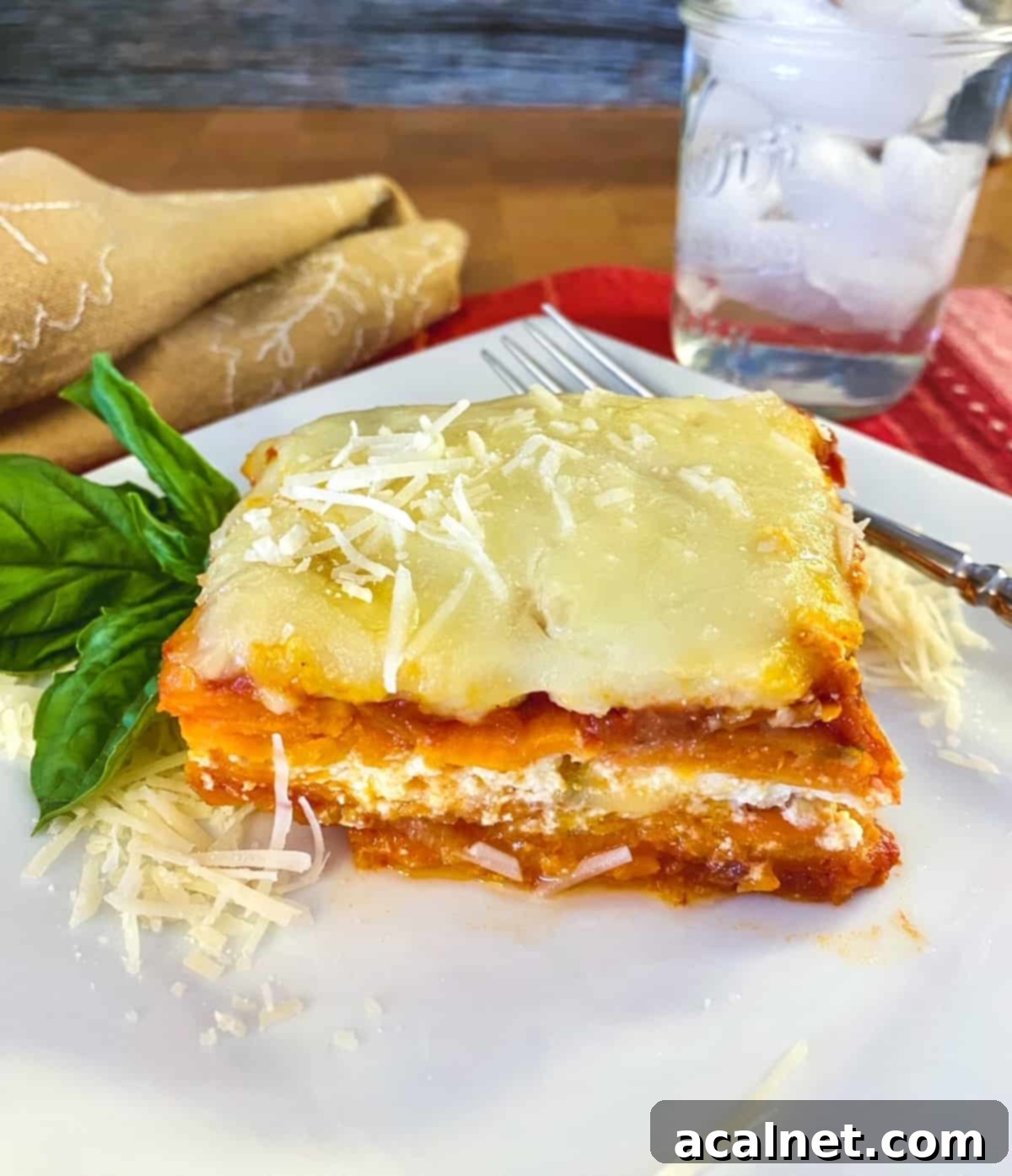 Sweet Potato Lasagna Perfection 2 A generous serving of vibrant sweet potato lasagna on a white plate, with a glass of water positioned to the side.