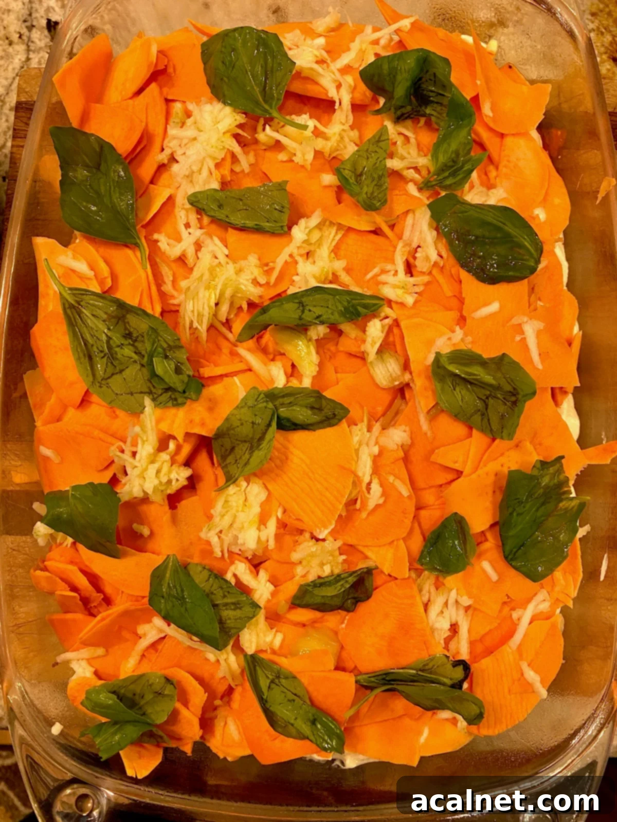 Sweet Potato Lasagna Perfection 11 Fresh, aromatic basil leaves laid atop a layer of thinly sliced sweet potatoes in a baking dish.