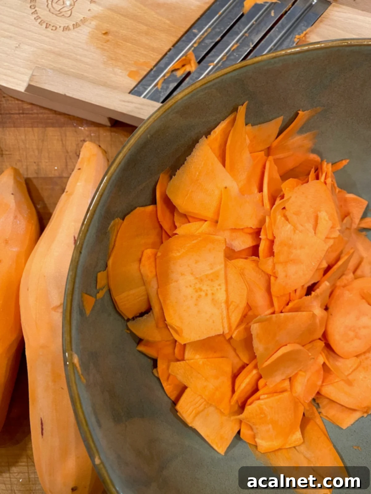 Sweet Potato Lasagna Perfection 14 A bowl filled with uniform, thinly sliced sweet potatoes, with several whole peeled sweet potatoes resting on the side, ready for slicing.