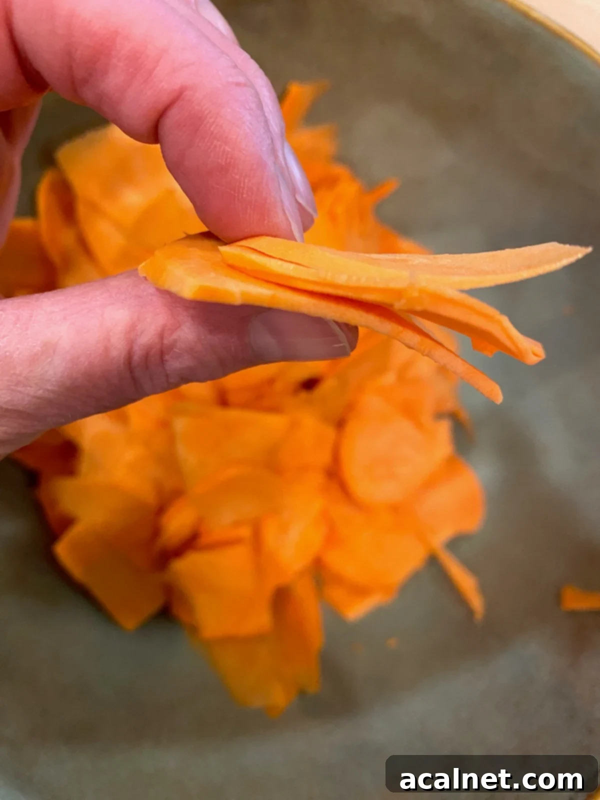 Sweet Potato Lasagna Perfection 15 A hand holding several translucent, thinly sliced sweet potato pieces, demonstrating the ideal thickness.
