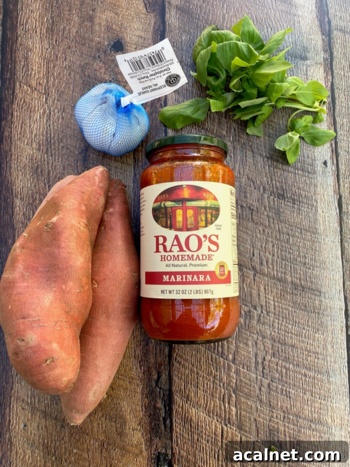 Sweet Potato Lasagna Perfection 4 Key ingredients for sweet potato lasagna artfully arranged on a rustic wooden plank: fresh sweet potatoes, a jar of rich marinara sauce, vibrant fresh basil leaves, and a large bulb of elephant garlic.