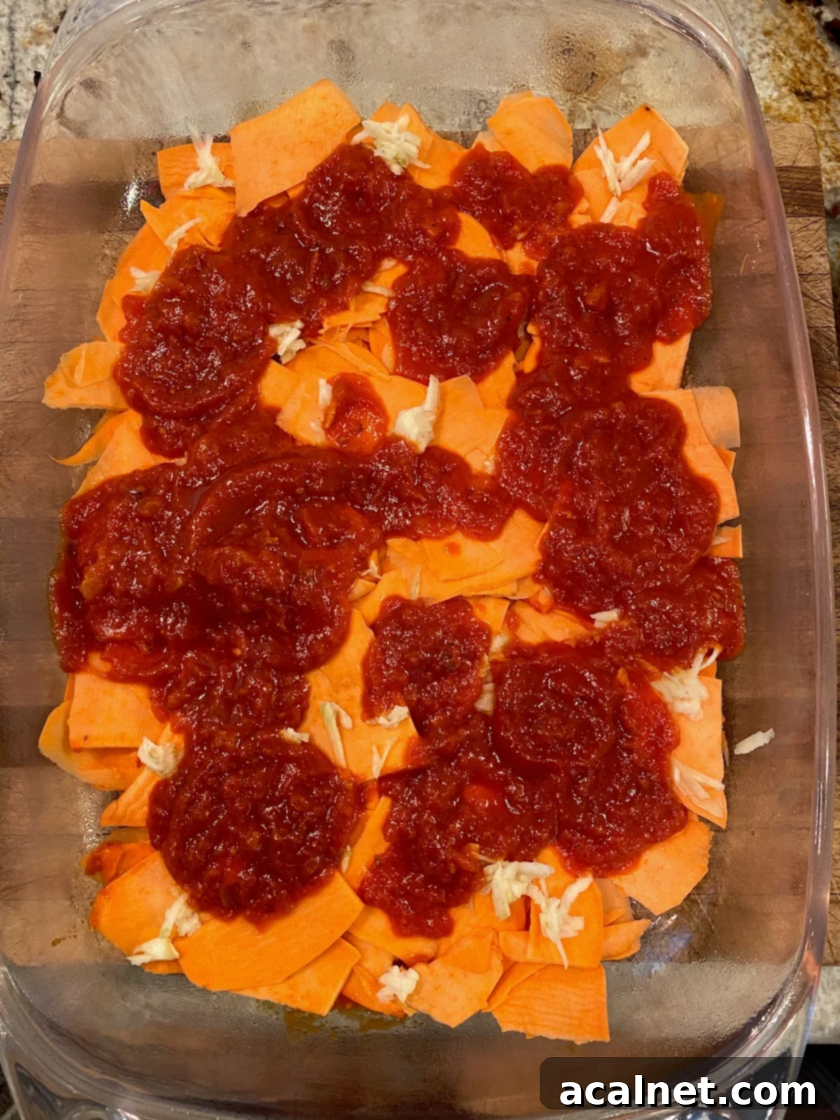 Sweet Potato Lasagna Perfection 9 A vibrant layer of marinara sauce spread over thinly sliced sweet potatoes in a glass baking dish.