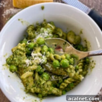 Pesto pasta salad being served from a bowl with parmesan cheese on top