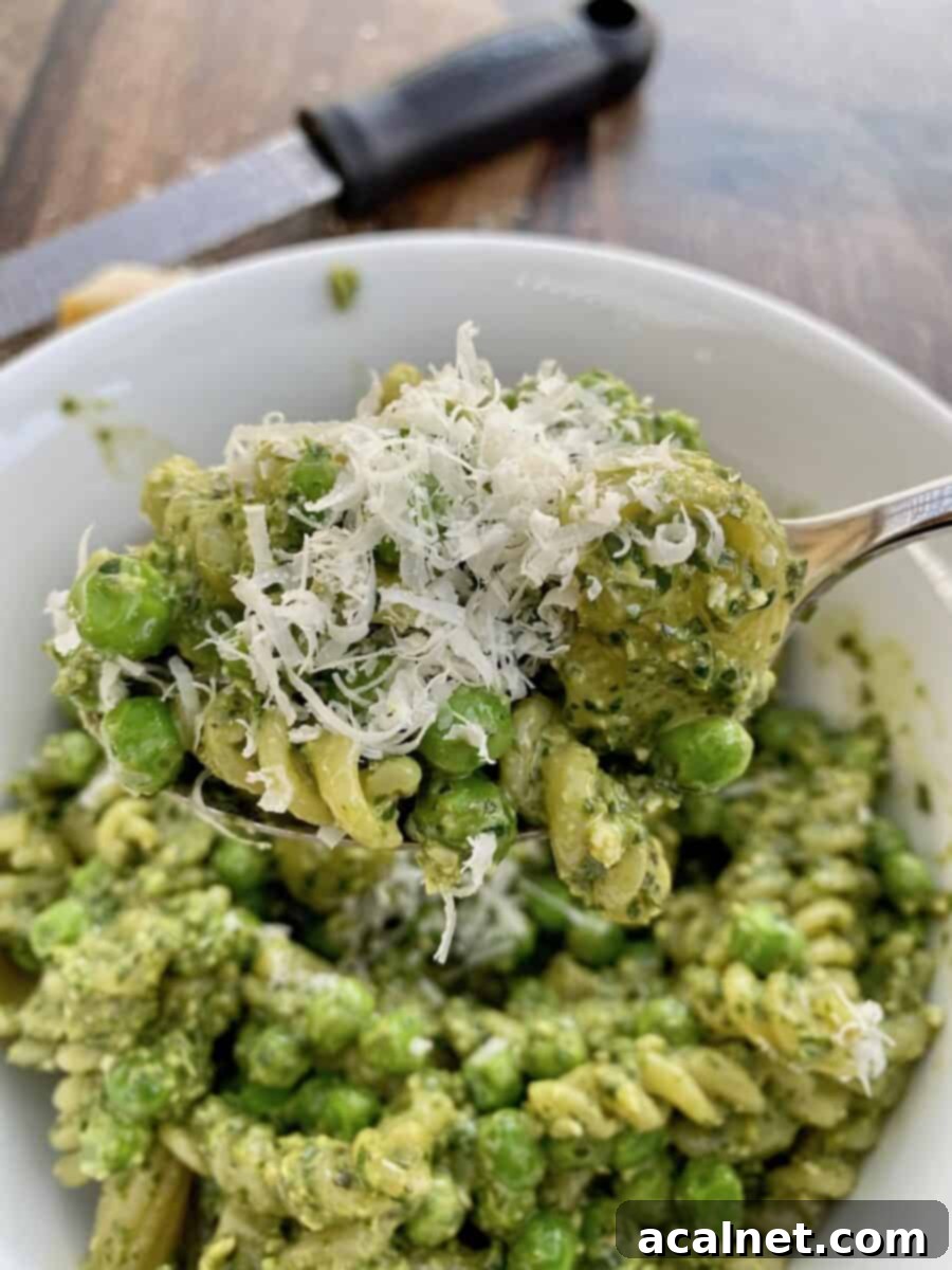 A bowl of pesto pasta salad with parmesan cheese shredded on top, ready to be served