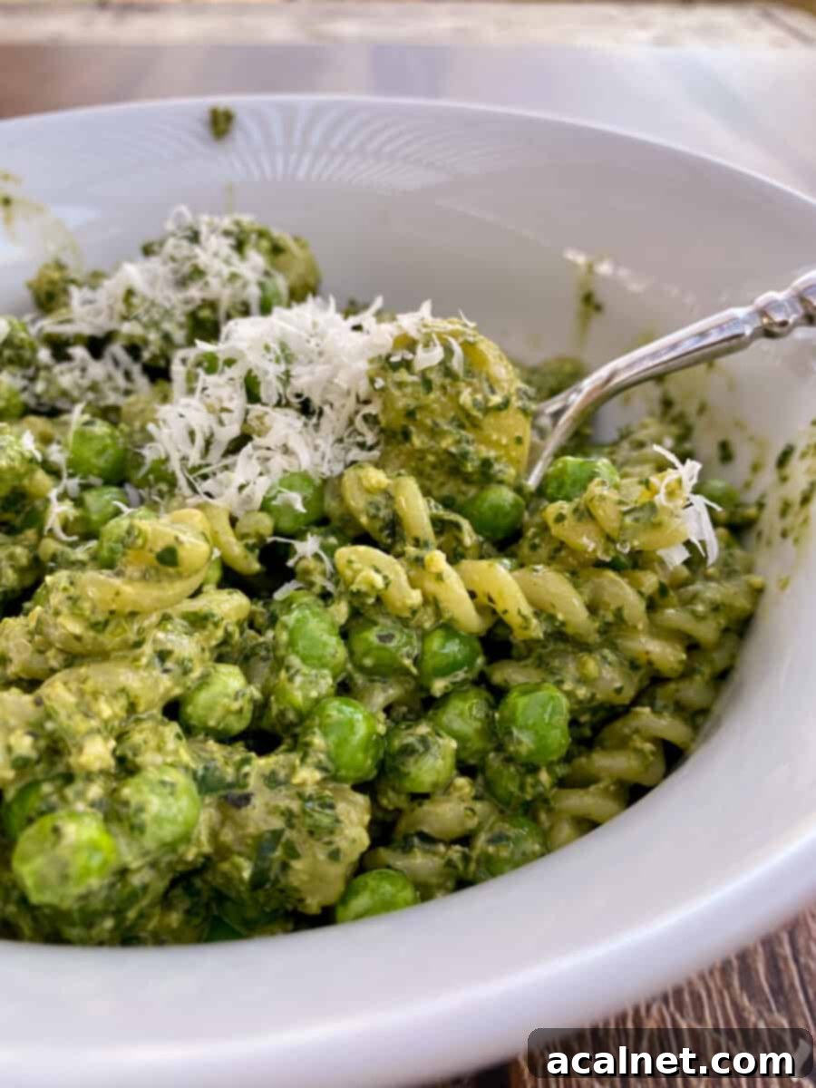 A full bowl of pesto pasta salad with a serving spoon on the side, ready for guests