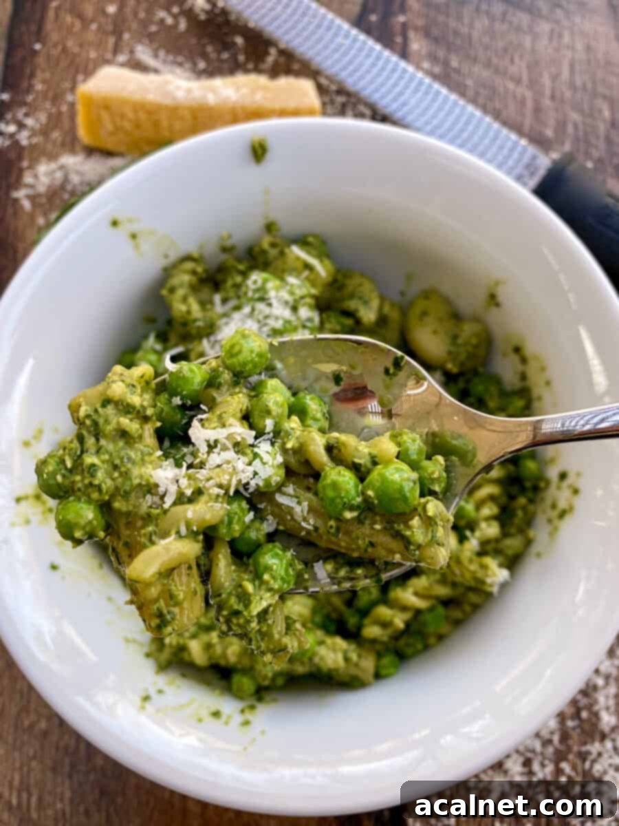 Pesto pasta salad being served from a bowl with parmesan cheese on top, ready for a meal