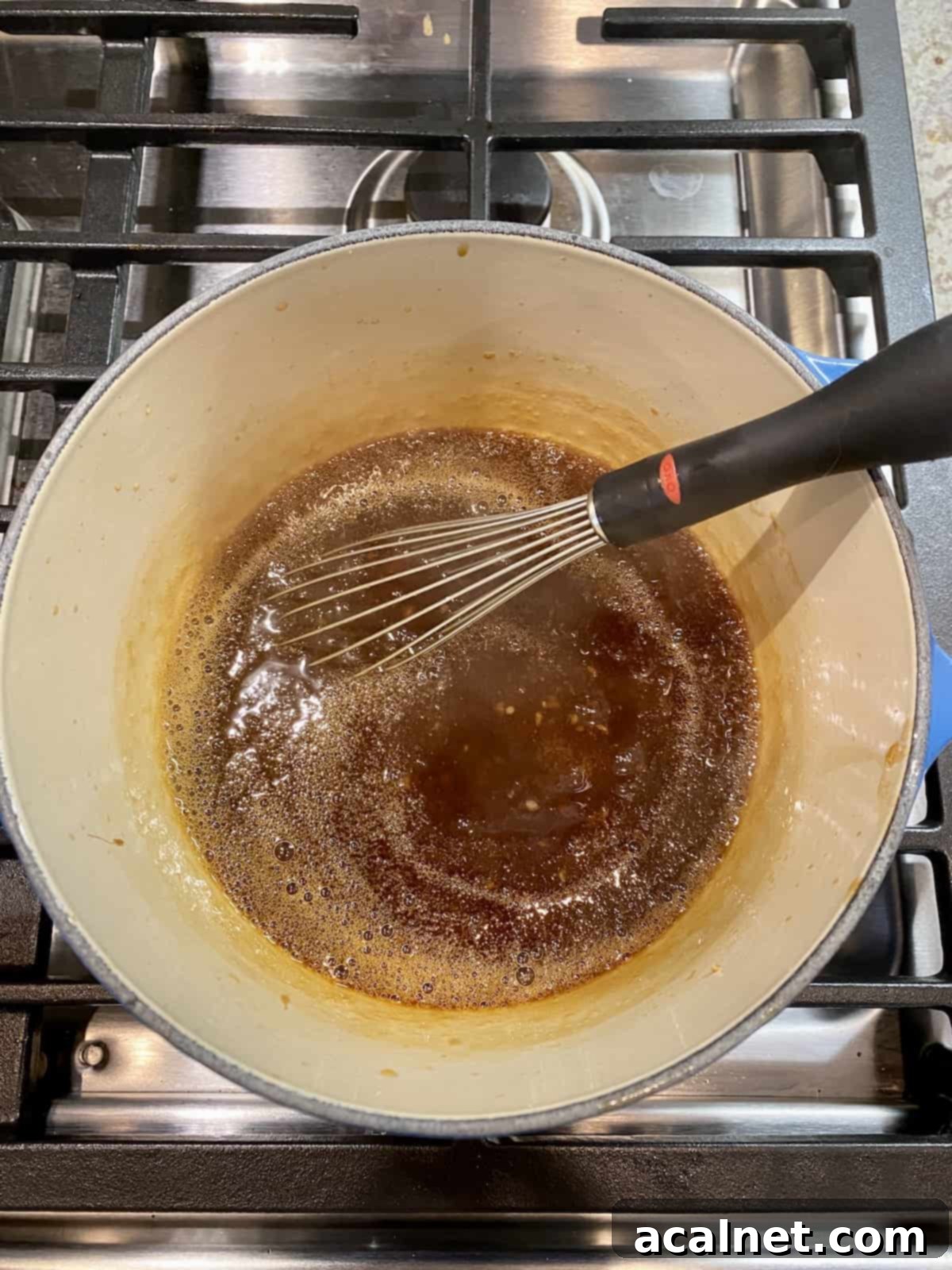 Orange sauce simmering in a saucepan on the stove, with a metal whisk resting beside it.