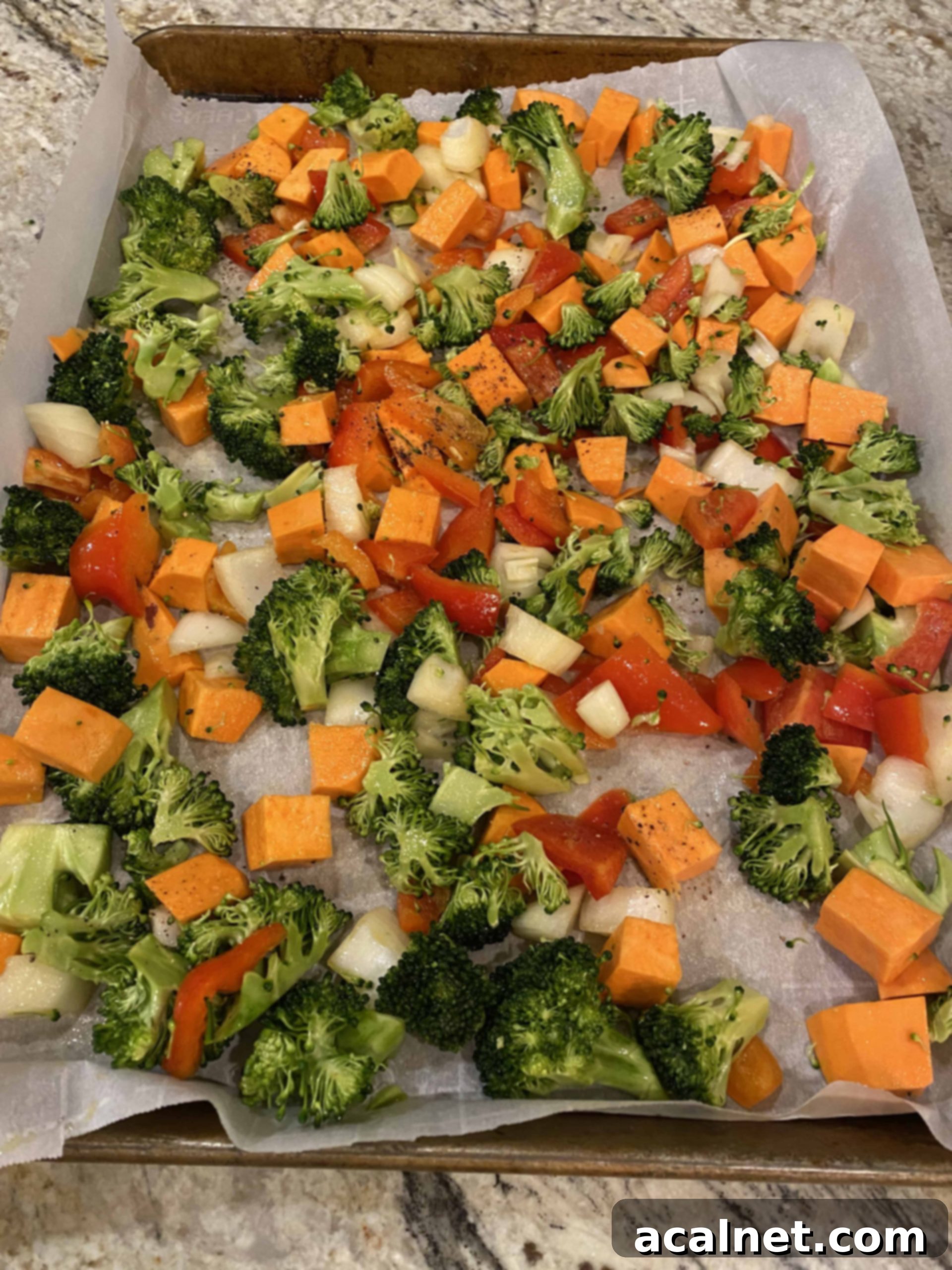 A mix of chopped broccoli florets and carrot slices spread out on parchment paper on a baking sheet, ready for roasting.
