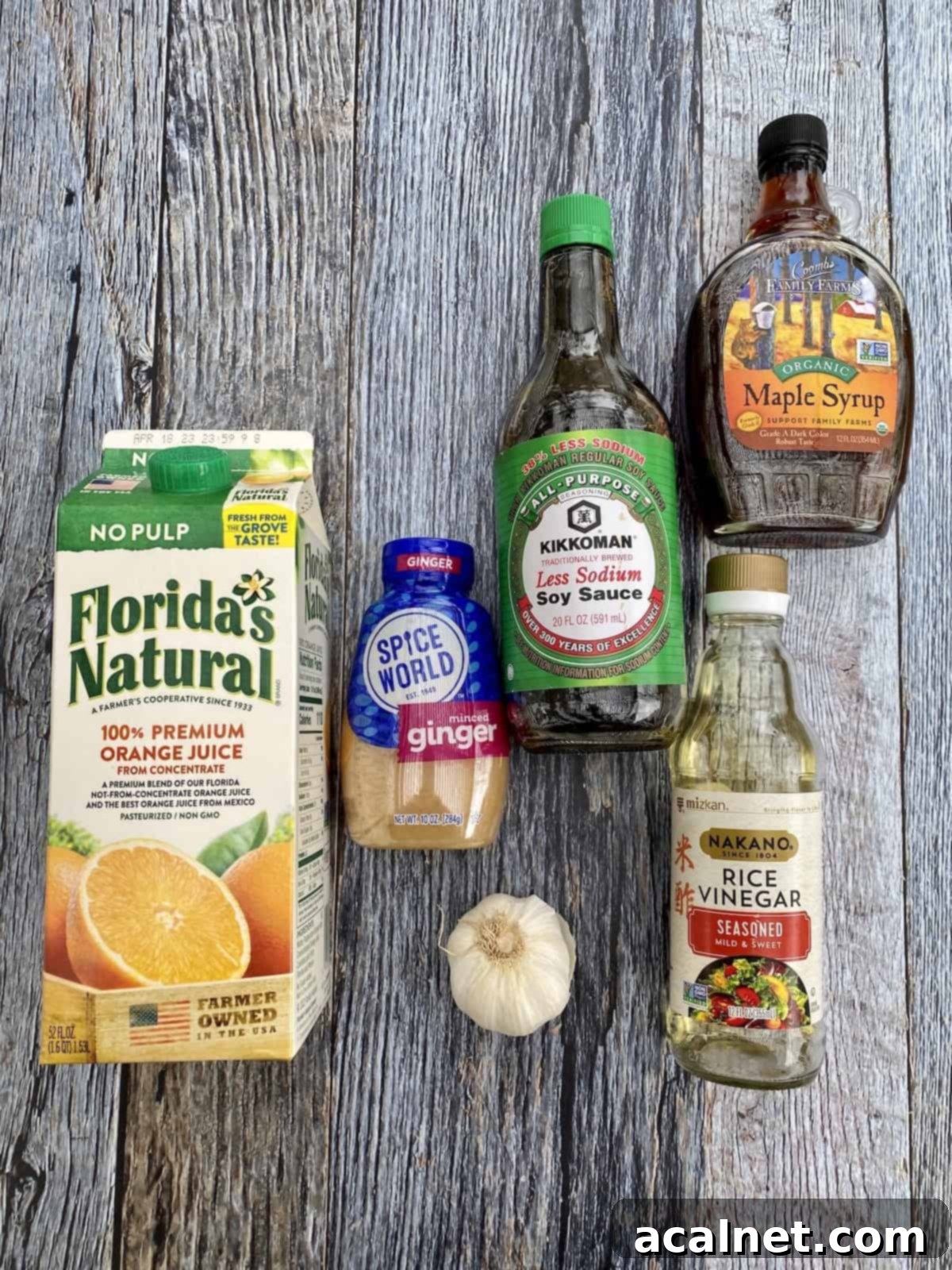 Orange sauce ingredients like orange juice, maple syrup, soy sauce, and ginger arranged on a wooden board.
