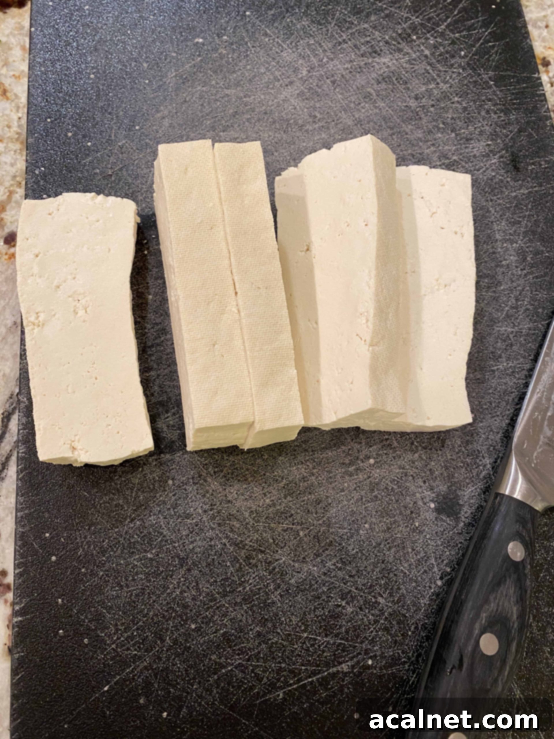 Thick, uniform slices of uncooked, pressed tofu on a cutting board.