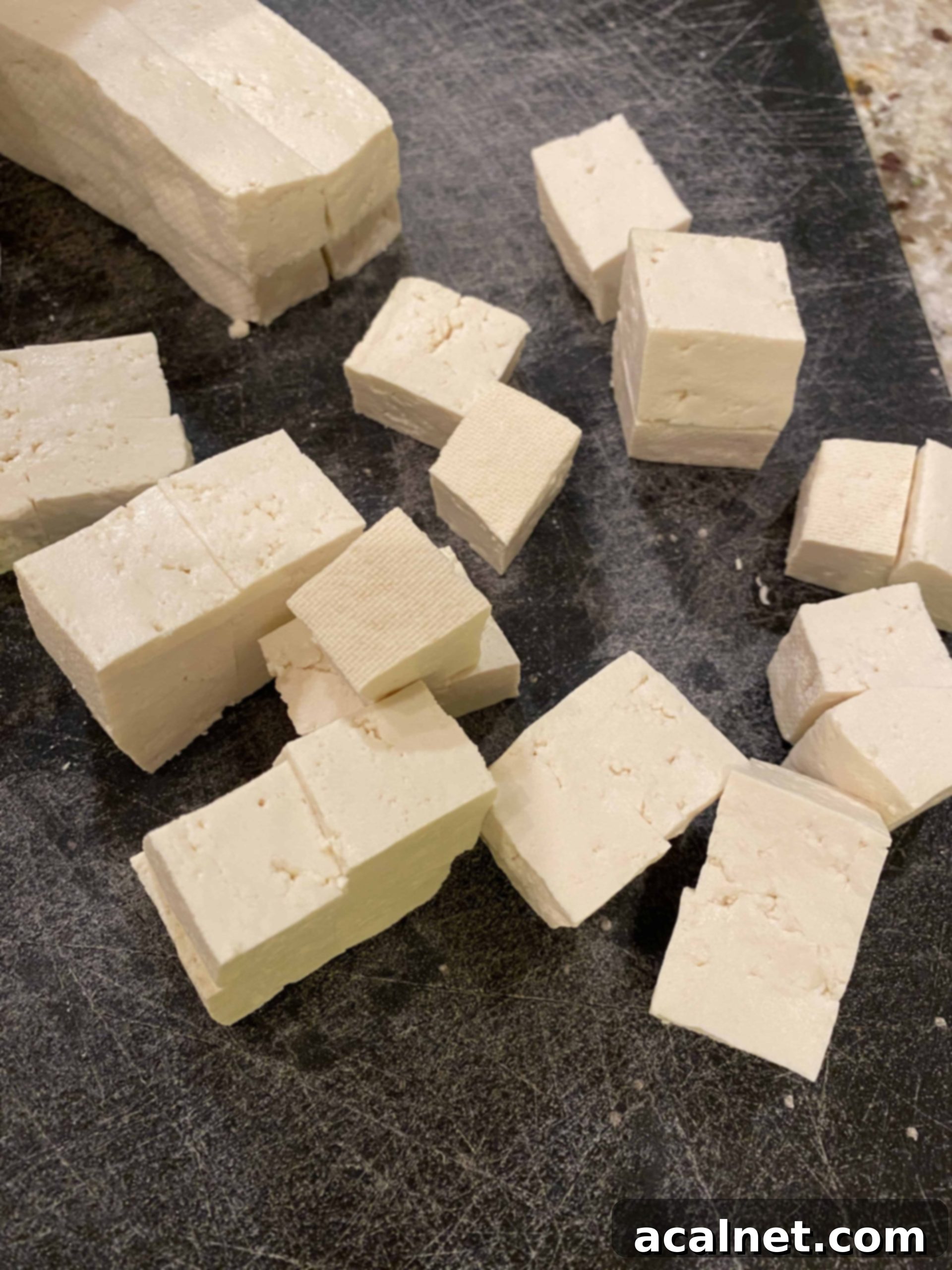 Diced tofu pieces, approximately one inch cubes, on a cutting board.